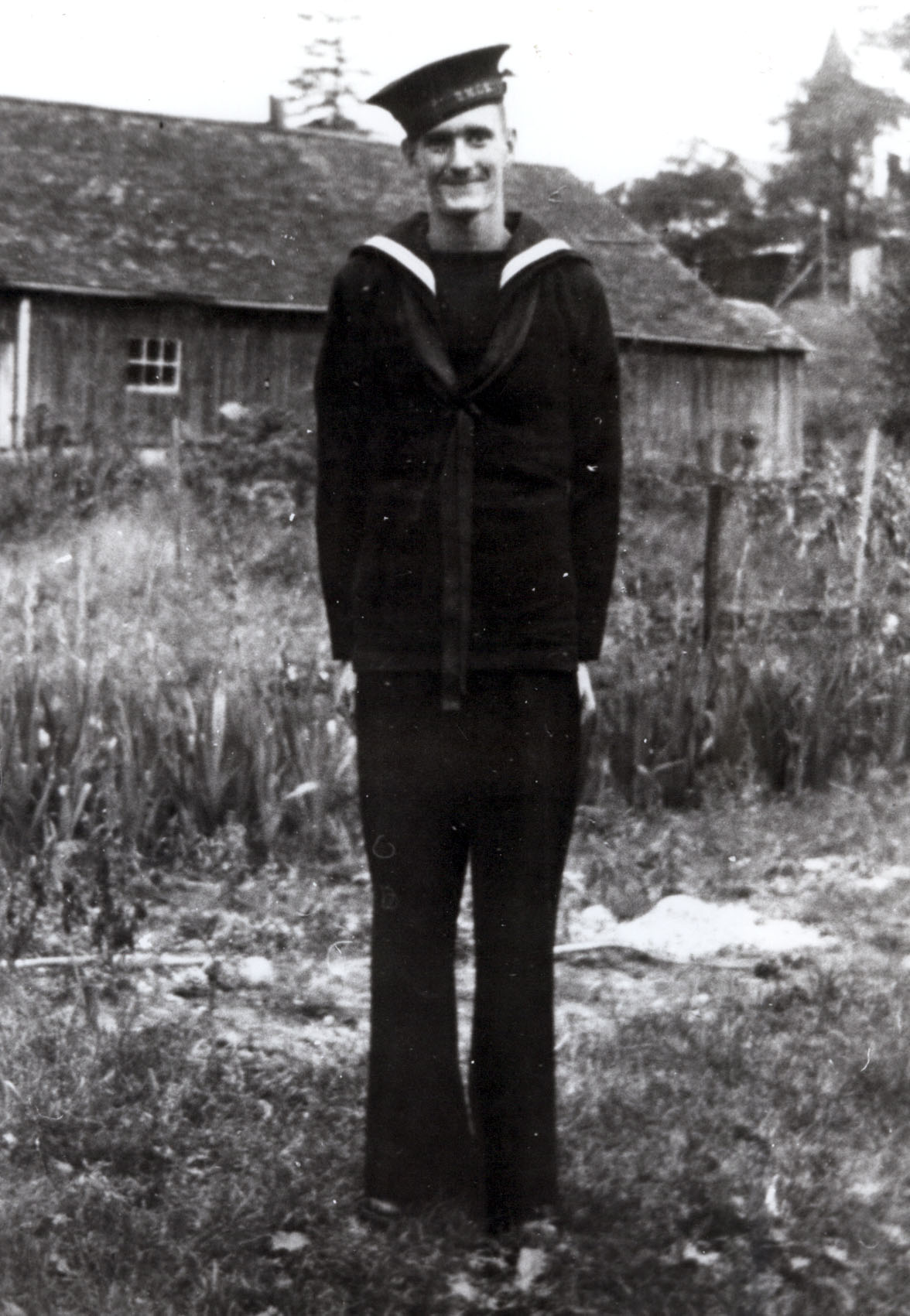 Byard Donnelly stands in his World War two naval uniform in front of a wood plank home.